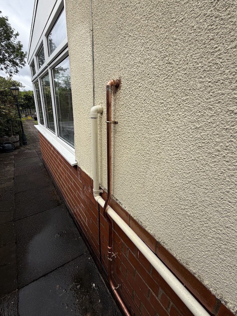 A copper pipe run down a pebbledash wall with two soldered bends, clipped straight.