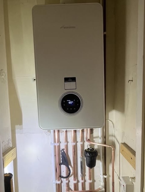 A new Worcester boiler on a wall with a rank of copper pipe drops beneath it, the display reading 65 degrees.